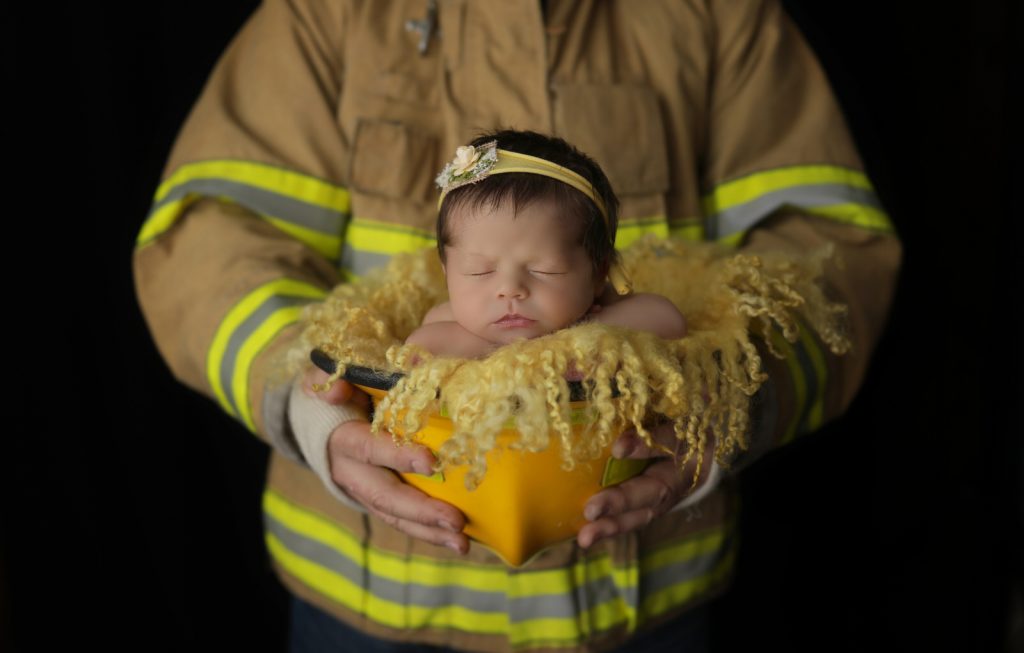 Firefighter dad poses with baby in his helmet during newborn session with harrisburg pa newborn photographer