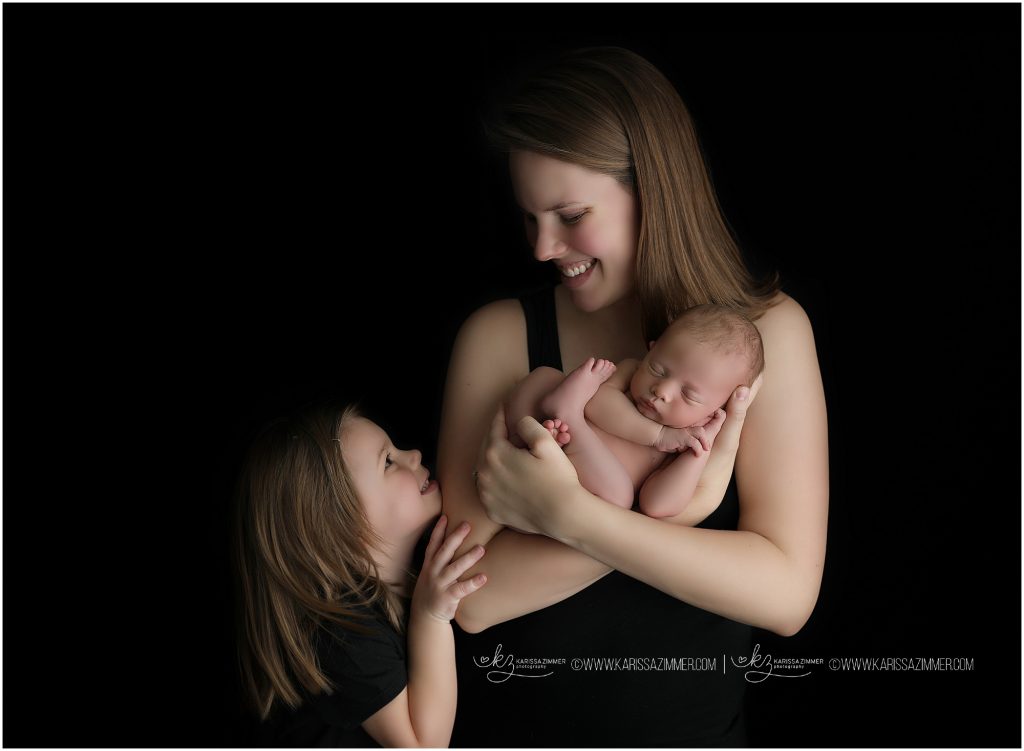 mom cuddles newborn baby boy as big sister snuggles in during photo session