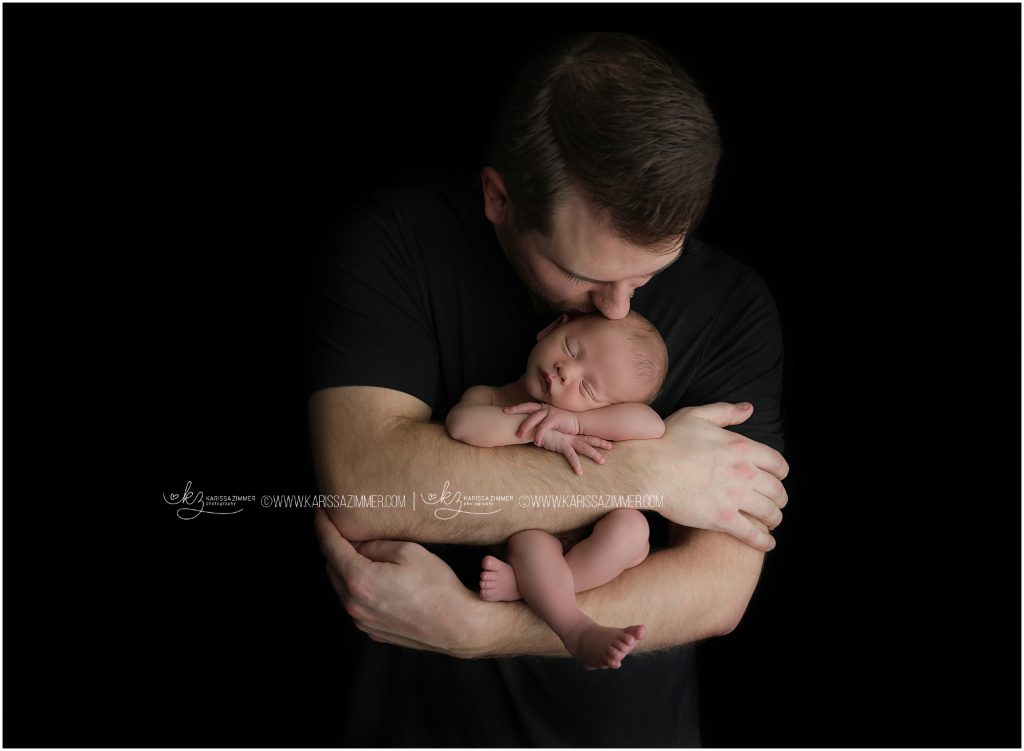 dad kisses newborn baby boy on head in camp hill pa during newborn photo shoot