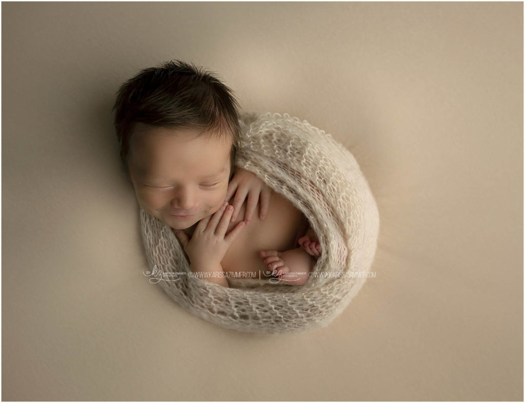 newborn baby boy smiles while posed at his newborn photo session 