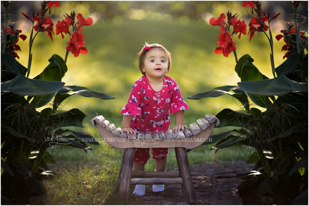 one year old baby girl stands with photo prop during her photo session with karissa zimmer photography
