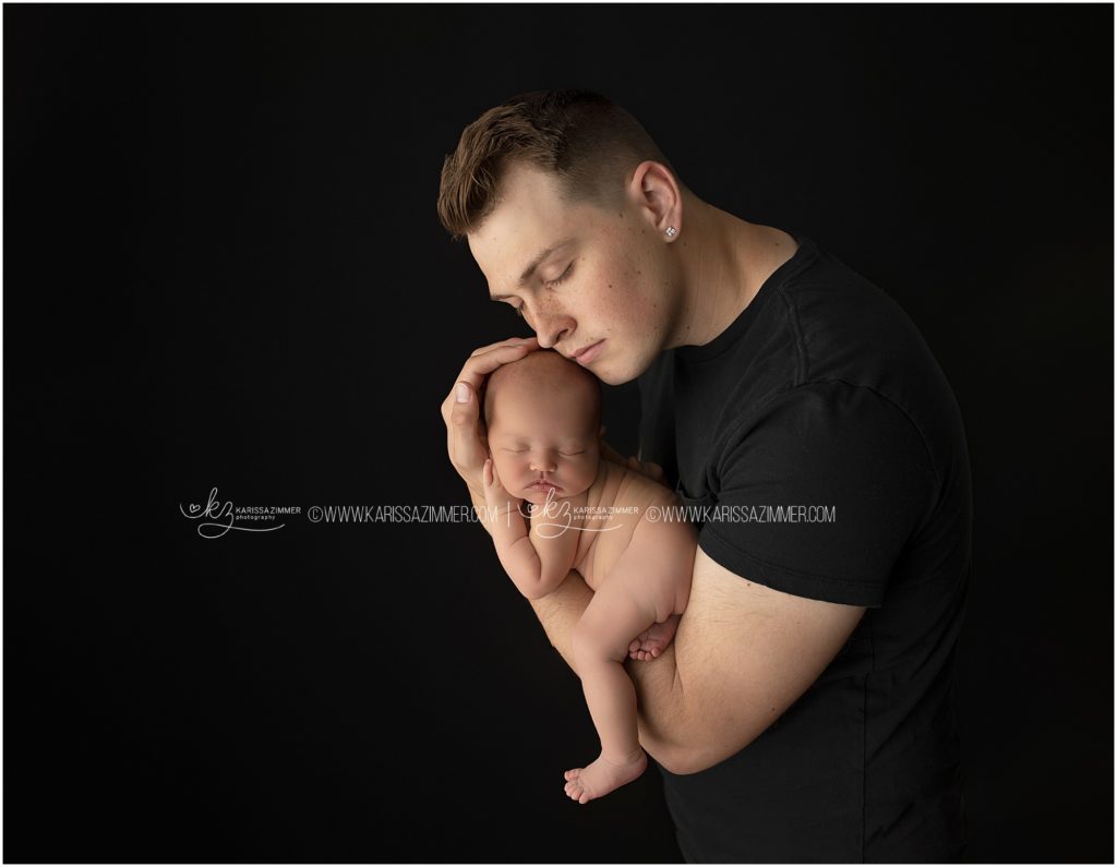 new father poses with newborn daughter at studio newborn photography session near 17050