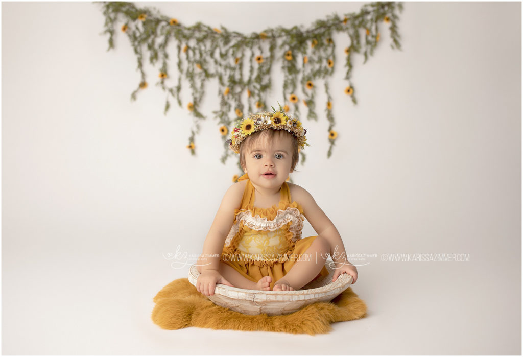 little girl wears yellow romper and poses in bowl for her first birthday photos