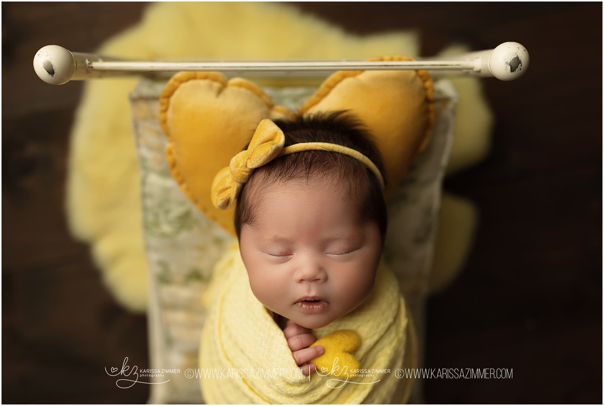Newborn baby girl in yellow on little bed prop