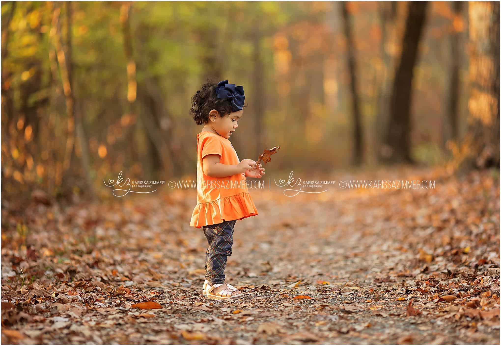 A little girl explores outdoors and examines a leaf at her family photoshoot