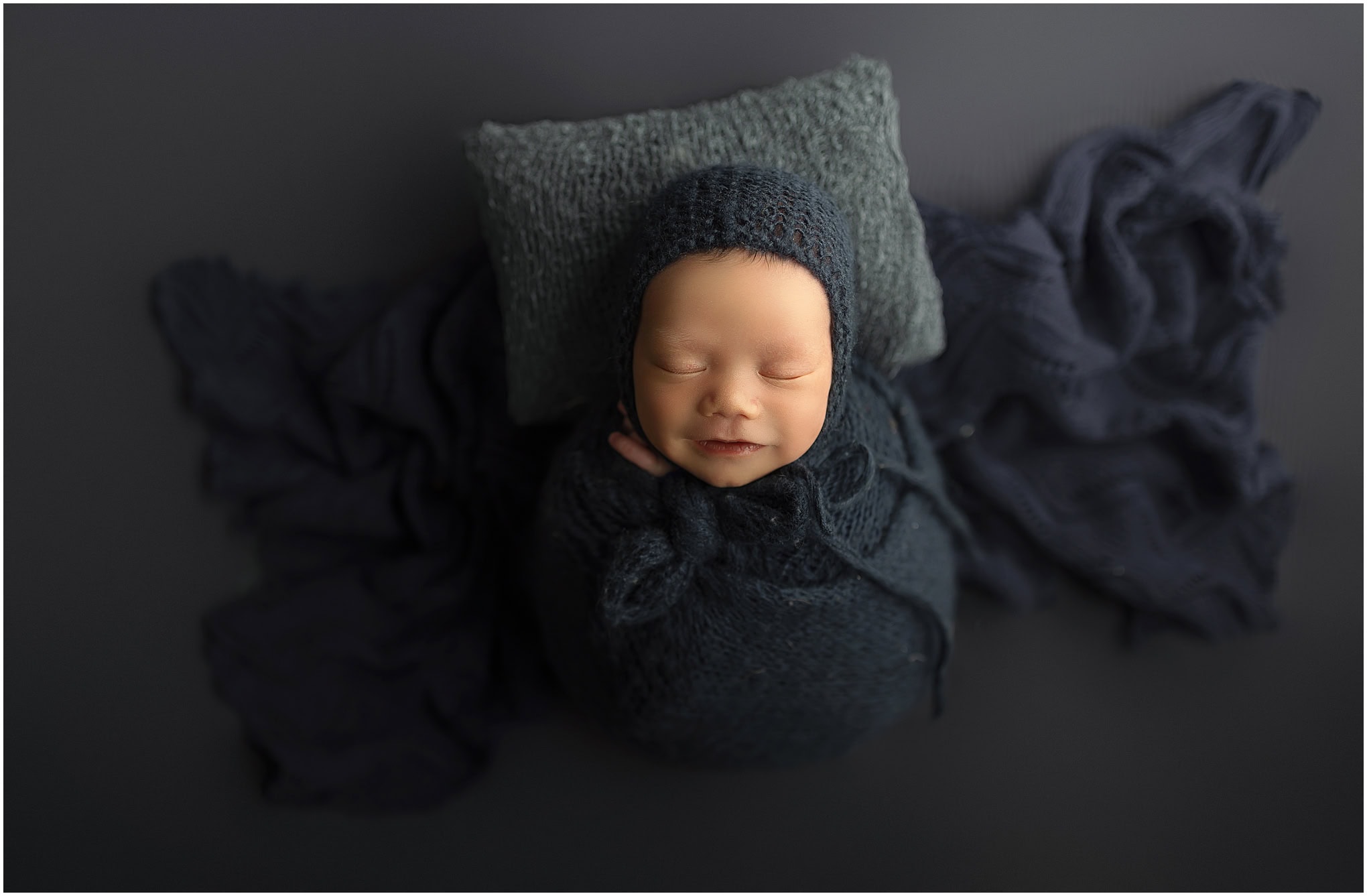 A sleeping newborn baby boy displays a sweet little smile during his studio newborn photo session.