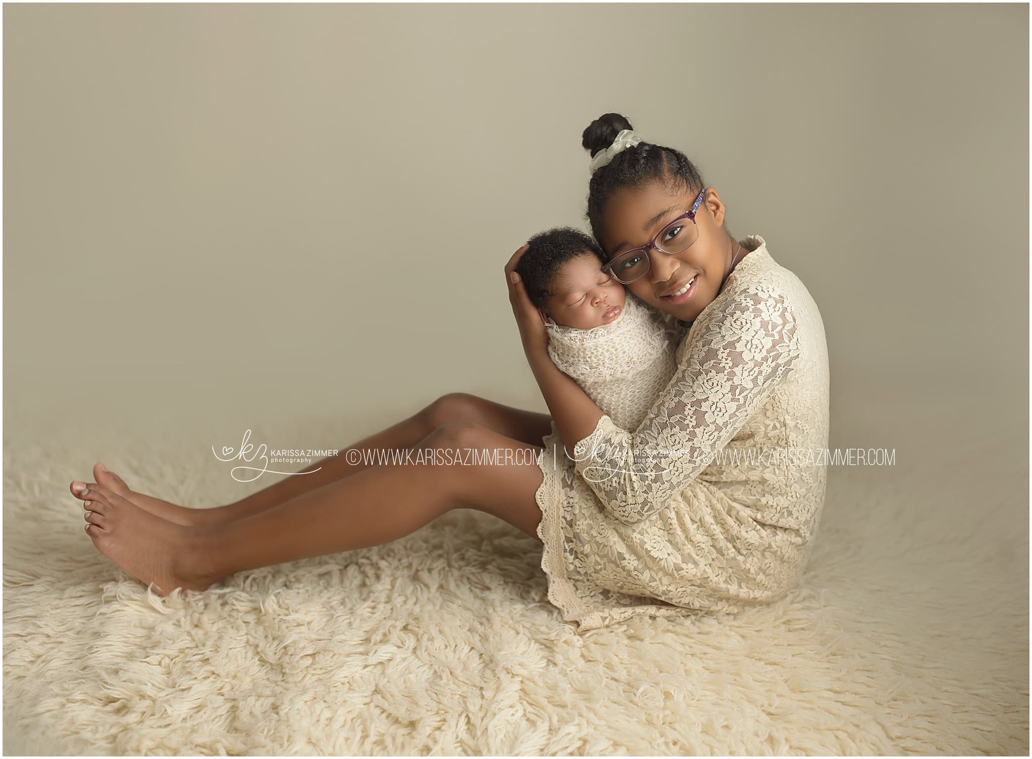 A big sister poses with her newborn baby brother on a light backdrop in Harrisburg newborn photography studio