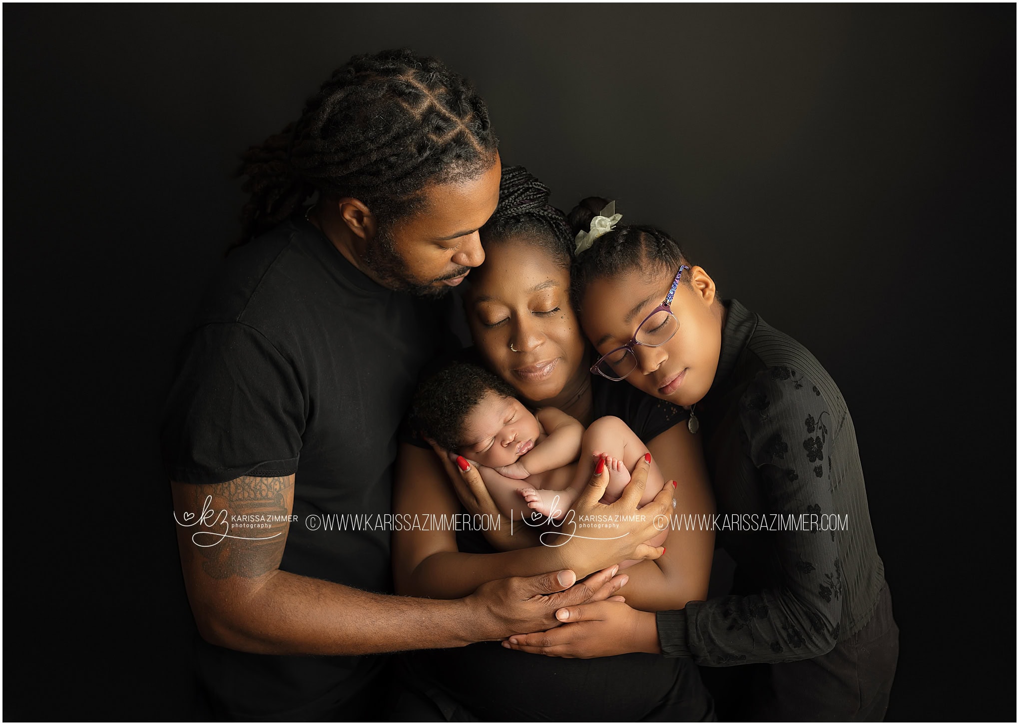 A mom, dad, and big sister pose on a black backdrop for their first portrait as a family of 4 in a Harrisburg newborn studio