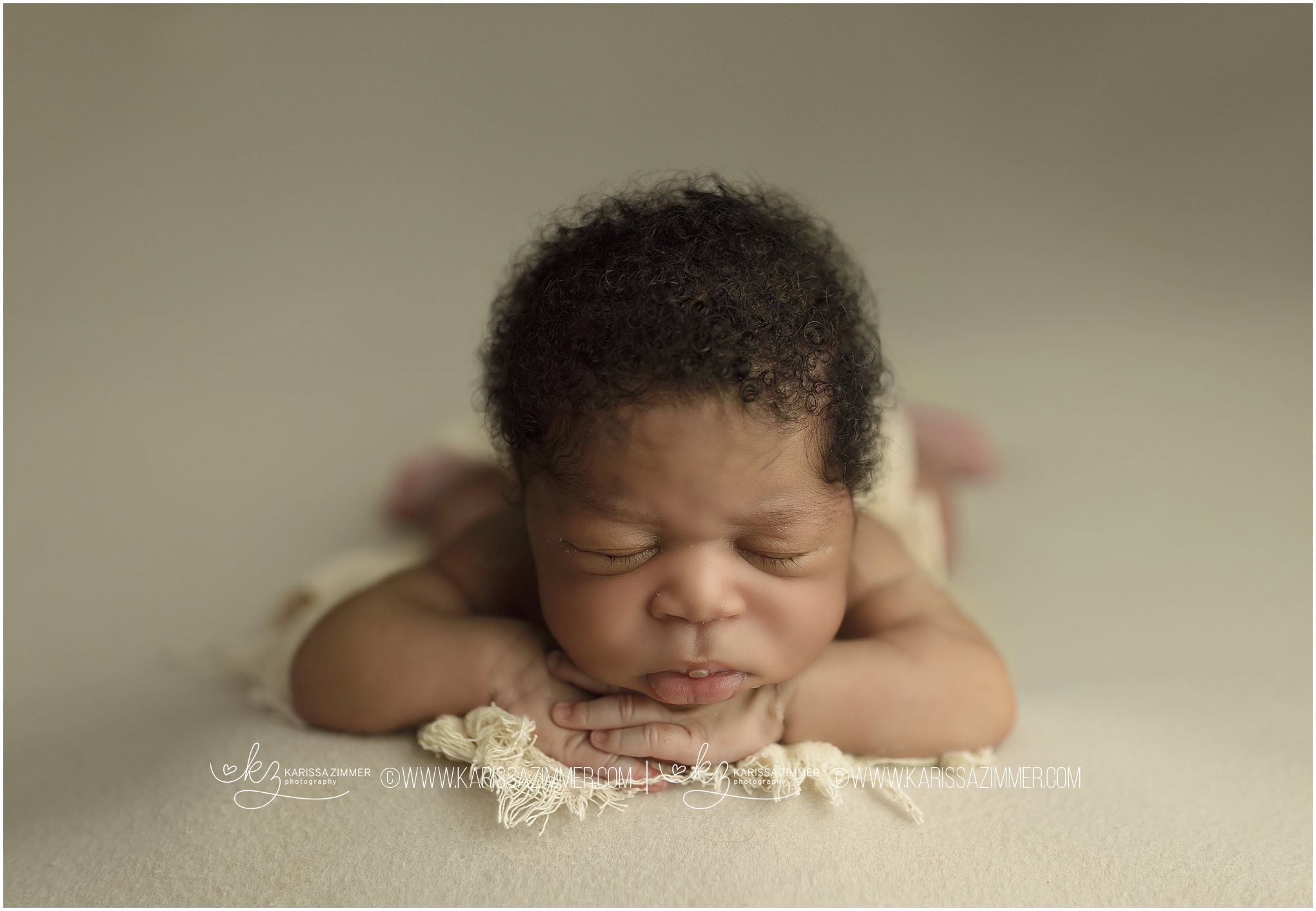 Newborn baby boy sleeps soundly while posed on a cream backdrop at Karissa Zimmer Photography newborn studio