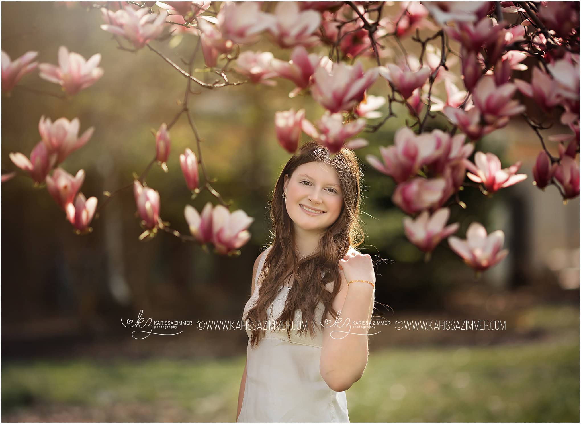 Senior girl poses by a flowering tree for her outdoor photos