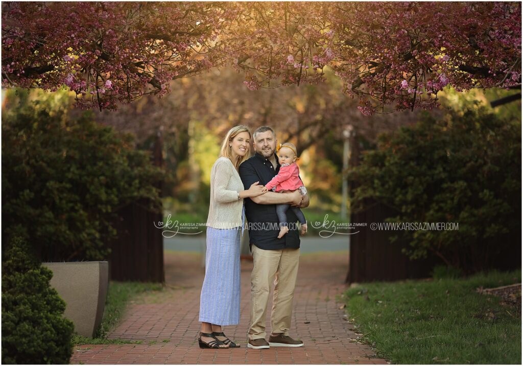 A family of 3 pose together during their outdoor family photo session near 17050