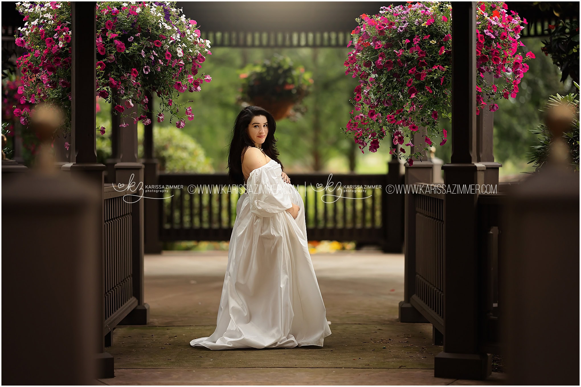 An expecting mother poses in a flowy white dress at her outdoor pregnancy photoshoot 