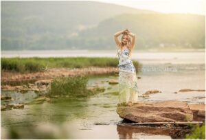 A high school girl poses on a rock in the Susquehanna River during her senior photoshoot.