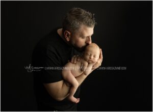 A new father poses with his newborn baby daughter on his arm during their newborn photo session near 17055