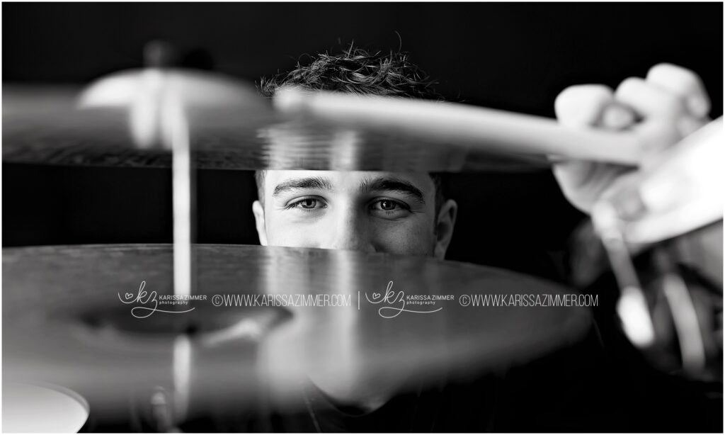 High school senior boy peeks through his drum cymbals for a creative studio photoshoot near Hershey PA