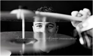 High school senior boy peeks through his drum cymbals for a creative studio photoshoot near Hershey PA
