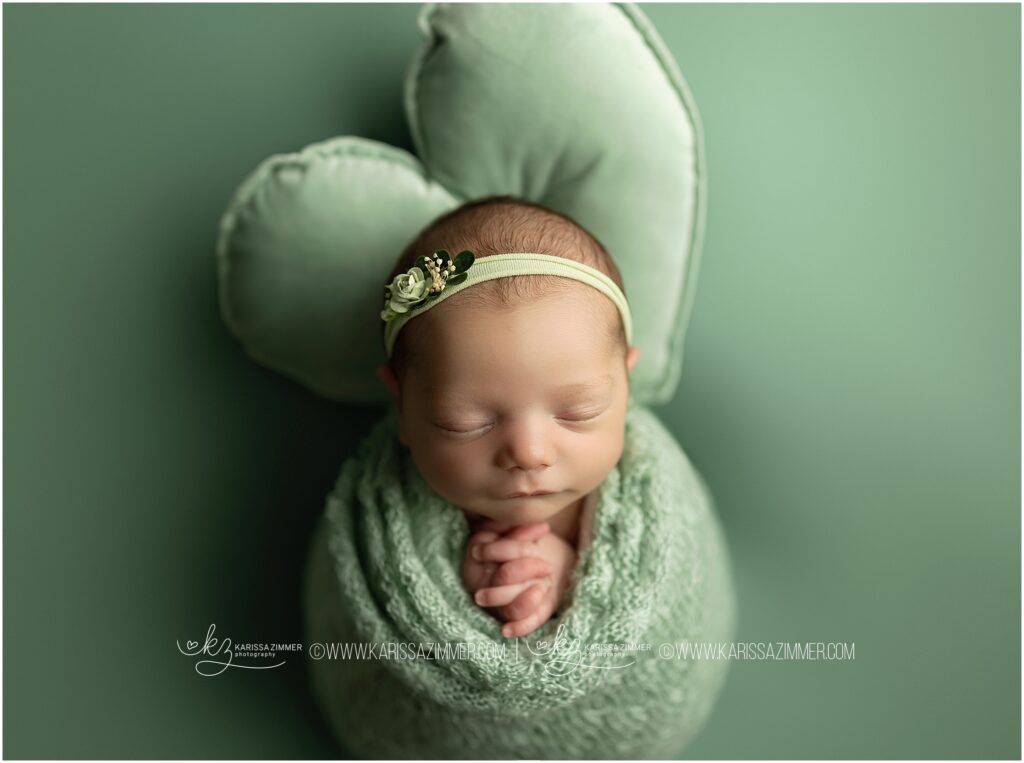 Baby girl is photographed on green with her hands in the praying postition